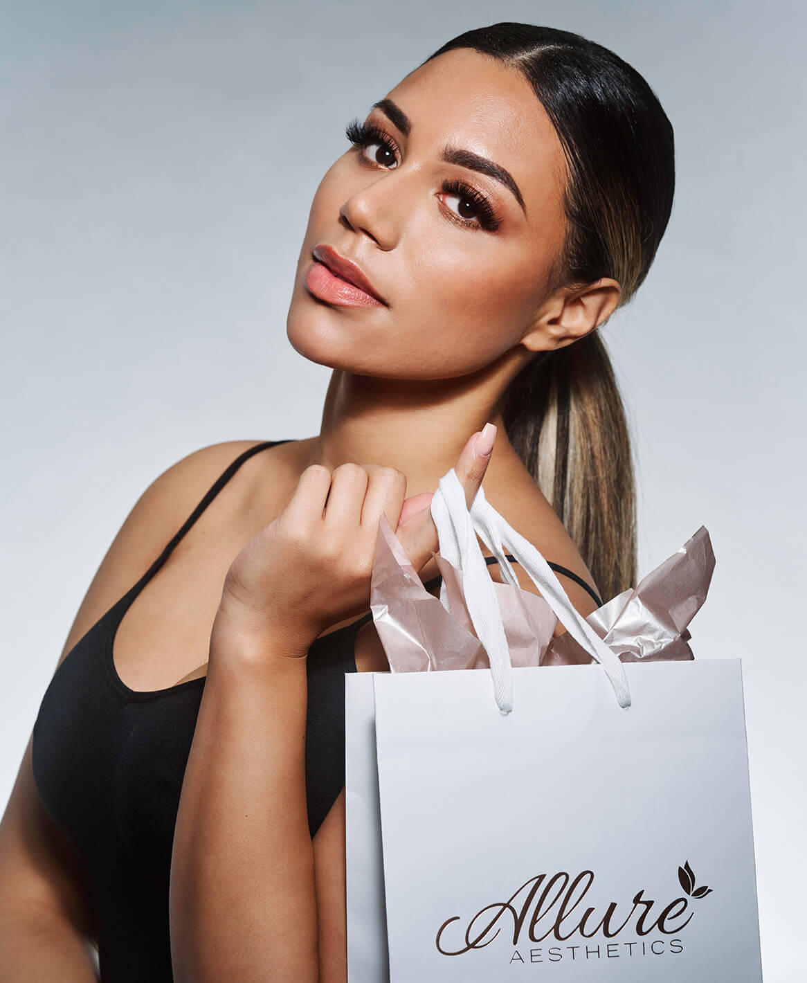 Woman posing with an Allure Aesthetics shopping bag, representing luxury aesthetic treatments and products.