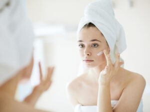 Woman applying anti-aging peptide cream to her face in front of mirror